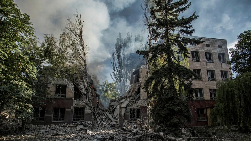 Seorang wanita berjalan melewati kawah cangkang di depan bangunan tempat tinggal yang rusak di kota Siversk, wilayah Donetsk. (AFP via Getty Images/ANATOLII STEPANOV)