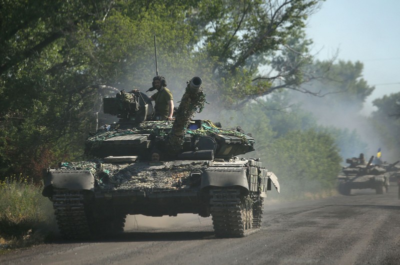 Seorang wanita berjalan melewati kawah cangkang di depan bangunan tempat tinggal yang rusak di kota Siversk, wilayah Donetsk. (AFP via Getty Images/ANATOLII STEPANOV)