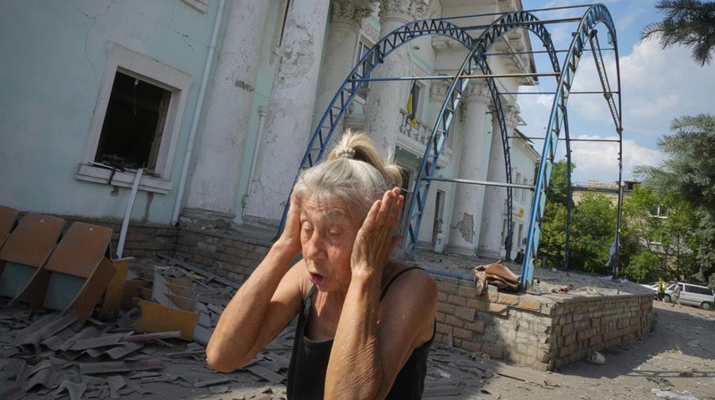 Seorang wanita berjalan melewati kawah cangkang di depan bangunan tempat tinggal yang rusak di kota Siversk, wilayah Donetsk. (AFP via Getty Images/ANATOLII STEPANOV)