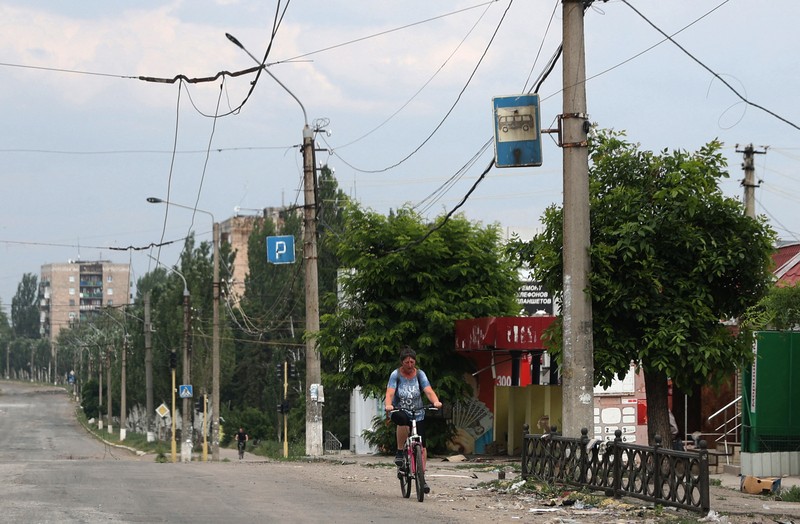 Seorang wanita berjalan melewati kawah cangkang di depan bangunan tempat tinggal yang rusak di kota Siversk, wilayah Donetsk. (AFP via Getty Images/ANATOLII STEPANOV)