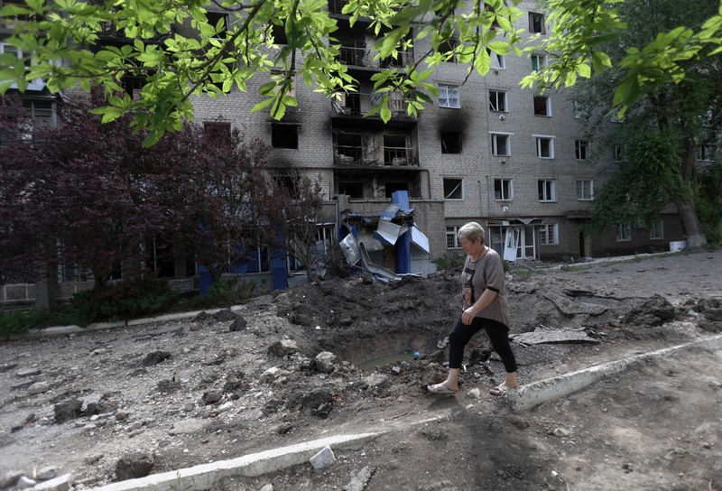 Seorang wanita berjalan melewati kawah cangkang di depan bangunan tempat tinggal yang rusak di kota Siversk, wilayah Donetsk. (AFP via Getty Images/ANATOLII STEPANOV) Seorang wanita berjalan melewati kawah cangkang di depan bangunan tempat tinggal yang rusak di kota Siversk, wilayah Donetsk. (AFP via Getty Images/ANATOLII STEPANOV)