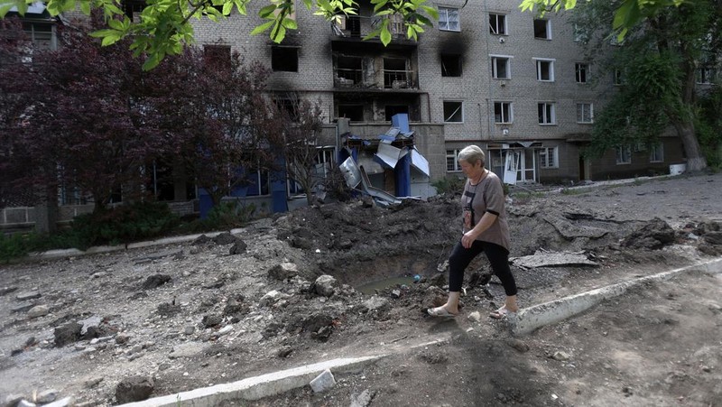 Seorang wanita berjalan melewati kawah cangkang di depan bangunan tempat tinggal yang rusak di kota Siversk, wilayah Donetsk. (AFP via Getty Images/ANATOLII STEPANOV)
