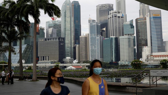 Warga yang memakai masker wajah melewati cakrawala kota selama wabah penyakit coronavirus (COVID-19), di Singapura. (REUTERS/EDGAR SU)
