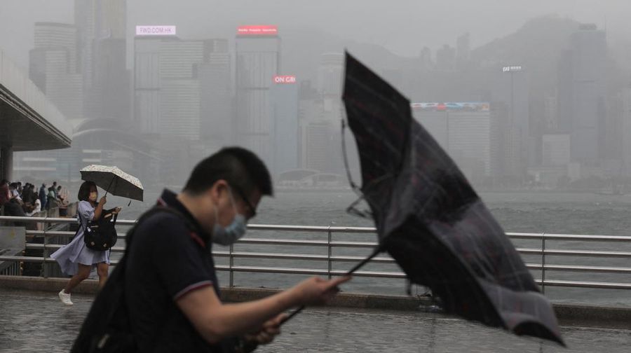 Orang-orang memegang payung di tengah hujan di tepi pantai, di tengah peringatan topan pada peringatan 25 tahun penyerahan bekas jajahan Inggris ke pemerintahan China, di Hong Kong. (REUTERS/PAUL YEUNG)g