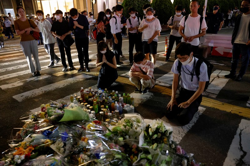 Japan Abe Shot People pray at a makeshift memorial at the scene where the former Prime Minister Shinzo Abe was shot while delivering his speech to support the Liberal Democratic Party's candidate during an election campaign in Nara, Friday, July 8, 2022. Abe, a divisive arch-conservative and one of his nation's most powerful and influential figures, has died after being shot during a campaign speech Friday in western Japan, hospital officials said.(Kyodo News via AP)