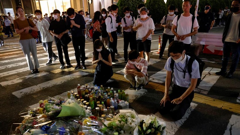 People pray at a makeshift memorial at the scene where the former Prime Minister Shinzo Abe was shot while delivering his speech to support the Liberal Democratic Party's candidate during an election campaign in Nara, Friday, July 8, 2022.  Abe, a divisive arch-conservative and one of his nation's most powerful and influential figures, has died after being shot during a campaign speech Friday in western Japan, hospital officials said.(Kyodo News via AP)