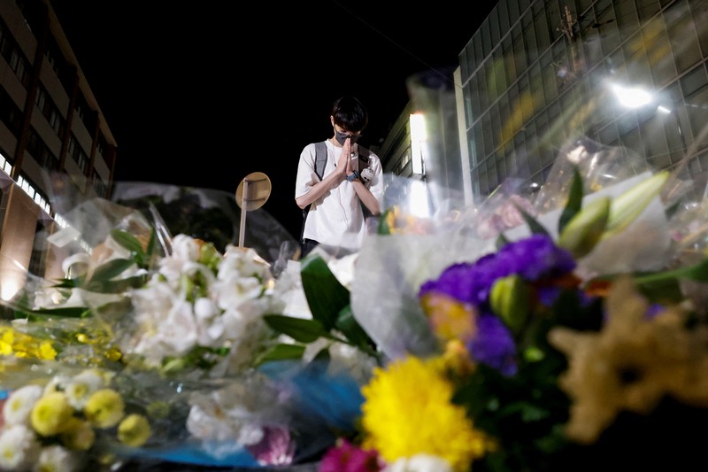 Japan Abe Shot People pray at a makeshift memorial at the scene where the former Prime Minister Shinzo Abe was shot while delivering his speech to support the Liberal Democratic Party's candidate during an election campaign in Nara, Friday, July 8, 2022. Abe, a divisive arch-conservative and one of his nation's most powerful and influential figures, has died after being shot during a campaign speech Friday in western Japan, hospital officials said.(Kyodo News via AP)