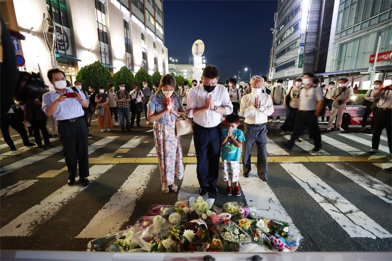People pray at a makeshift memorial at the scene where the former Prime Minister Shinzo Abe was shot while delivering his speech to support the Liberal Democratic Party's candidate during an election campaign in Nara, Friday, July 8, 2022.  Abe, a divisive arch-conservative and one of his nation's most powerful and influential figures, has died after being shot during a campaign speech Friday in western Japan, hospital officials said.(Kyodo News via AP)