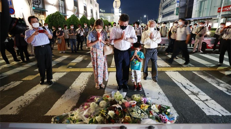 People pray at a makeshift memorial at the scene where the former Prime Minister Shinzo Abe was shot while delivering his speech to support the Liberal Democratic Party's candidate during an election campaign in Nara, Friday, July 8, 2022.  Abe, a divisive arch-conservative and one of his nation's most powerful and influential figures, has died after being shot during a campaign speech Friday in western Japan, hospital officials said.(Kyodo News via AP)