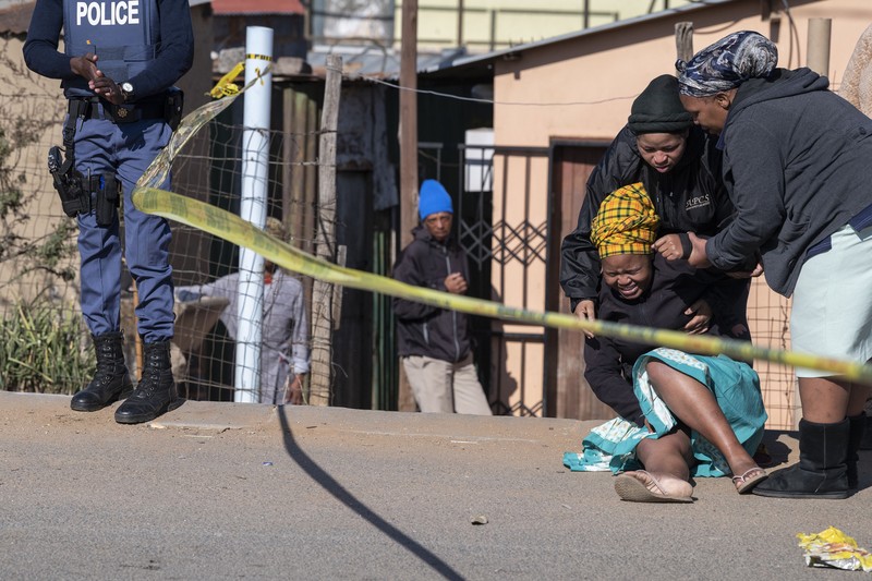 SOWETO, SOUTH AFRICA - JULY 10:  A woman reacts as securtiy forces and forensic service inspect the scene of a mass shooting in Soweto, South Africa, on July 10, 2022. Fourteen people have been killed in a mass shooting at a bar in Soweto township near Johannesburg, police said Sunday. (Photo by Ihsaan Haffejee/Anadolu Agency via Getty Images)