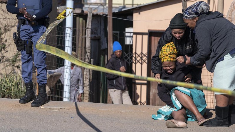 SOWETO, SOUTH AFRICA - JULY 10:  A woman reacts as securtiy forces and forensic service inspect the scene of a mass shooting in Soweto, South Africa, on July 10, 2022. Fourteen people have been killed in a mass shooting at a bar in Soweto township near Johannesburg, police said Sunday. (Photo by Ihsaan Haffejee/Anadolu Agency via Getty Images)
