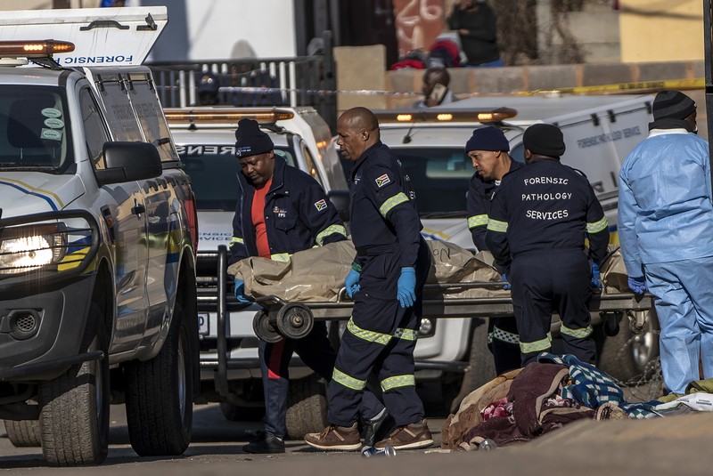 SOWETO, SOUTH AFRICA - JULY 10:  A woman reacts as securtiy forces and forensic service inspect the scene of a mass shooting in Soweto, South Africa, on July 10, 2022. Fourteen people have been killed in a mass shooting at a bar in Soweto township near Johannesburg, police said Sunday. (Photo by Ihsaan Haffejee/Anadolu Agency via Getty Images)