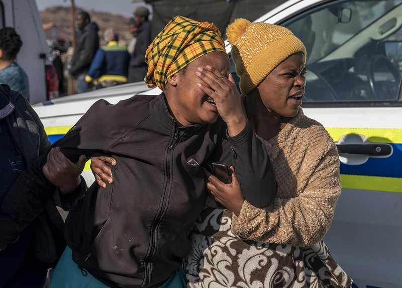 SOWETO, SOUTH AFRICA - JULY 10:  A woman reacts as securtiy forces and forensic service inspect the scene of a mass shooting in Soweto, South Africa, on July 10, 2022. Fourteen people have been killed in a mass shooting at a bar in Soweto township near Johannesburg, police said Sunday. (Photo by Ihsaan Haffejee/Anadolu Agency via Getty Images)