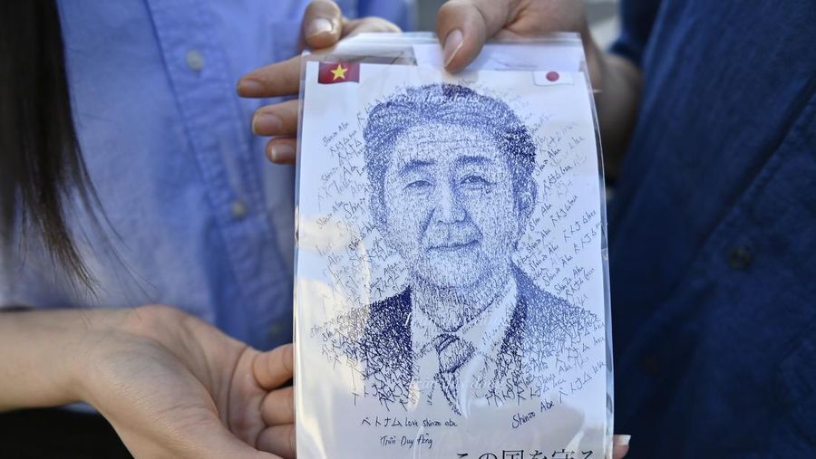 TOKYO, JAPAN - JULY 10 : A couple show an image representing the portrait of Shinzo Abe as they came pay homage in front of the residence of dead former Prime Minister of Japan Shinzo Abe on July 10, 2022 in Tokyo, Japan as body's Abe was transported from Nara city to Tokyo at his residence on previous morning. Shinzo Abe, Former Prime minister of Japan, was shot from behind during a street meeting to support a LDP (Liberal Democratic Party) candidate, on July 8, 2022 at Nara city, Japan during the campaign for the House of Councillors election set for July 10. (Photo by David Mareuil/Anadolu Agency via Getty Images)