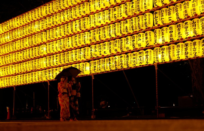Women in yukata, or casual summer kimonos, wearing protective mask amid the coronavirus disease (COVID-19) outbreak, walk between lanterns during the annual Mitama Festival at the Yasukuni Shrine, where more than 2.4 million war dead are enshrined, in Tokyo, Japan, July 13, 2022. REUTERS/Kim Kyung-Hoon