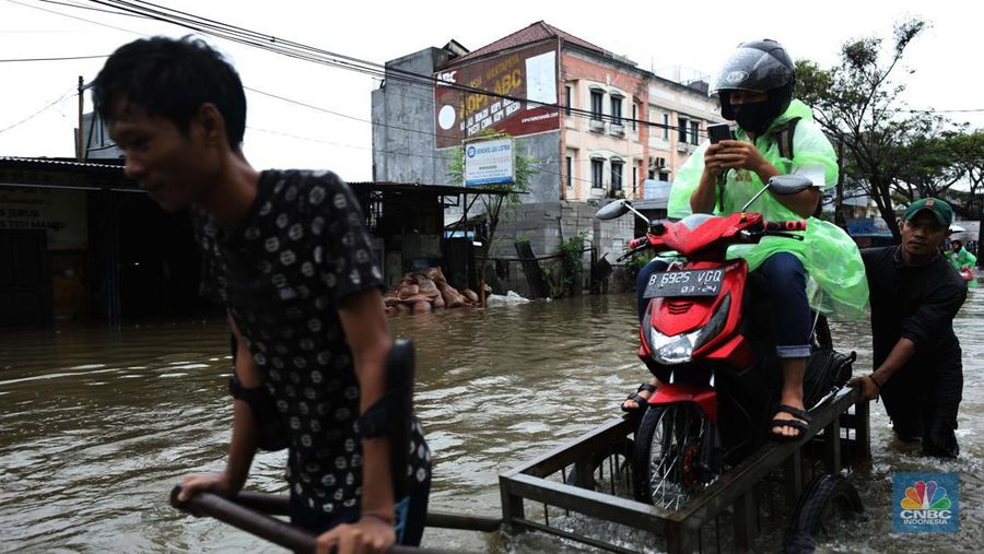 Pengendara sepeda motor menggunakan jasa gerobak saat melintasi banjir di Ciledug, Tangerang Banten, Sabtu (16/7/2022). (CNBC Indonesia/Tri Susilo)