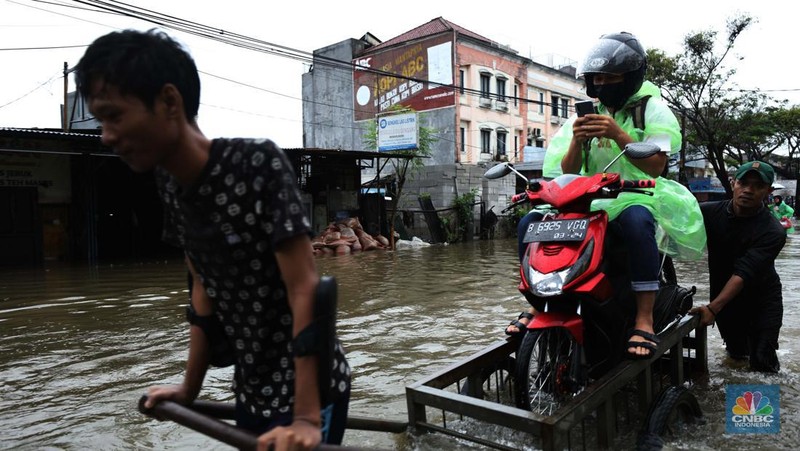 Pengendara sepeda motor menggunakan jasa gerobak saat melintasi banjir di Ciledug, Tangerang Banten, Sabtu (16/7/2022). (CNBC Indonesia/Tri Susilo)