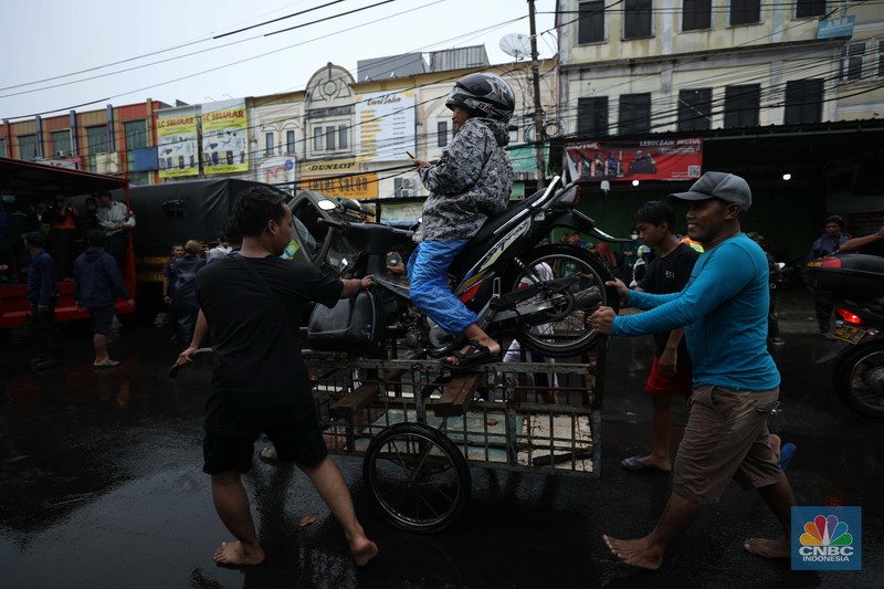 Pengendara sepeda motor menggunakan jasa gerobak saat melintasi banjir di Ciledug, Tangerang Banten, Sabtu (16/7/2022). (CNBC Indonesia/Tri Susilo)