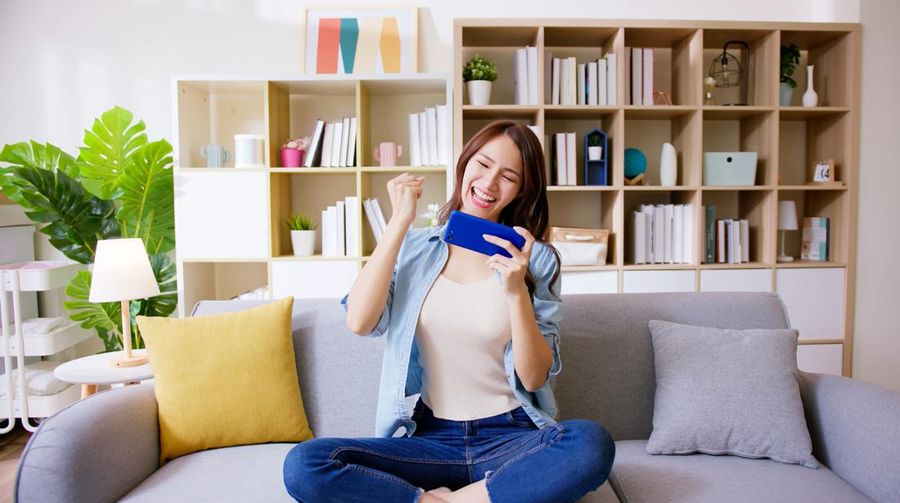 asian woman earns cryptocurrency from gami-fi or NFT mobile game and excited with fist gesture at home