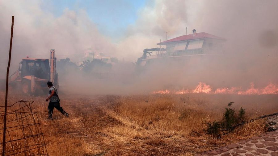 A person runs as wildfire approaches houses on Vatera coastal resort on the eastern island of Lesbos on July 23, 2022. - Residents were evacuated as the wilfire threatened properties. (Photo by Manolis LAGOUTARIS / AFP) (Photo by MANOLIS LAGOUTARIS/AFP via Getty Images)