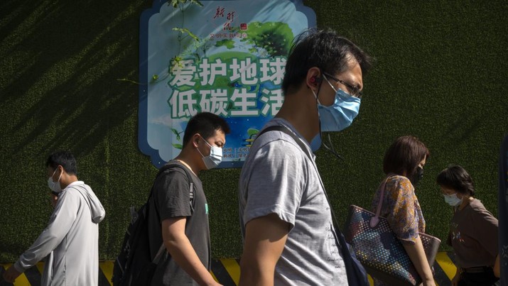 Commuters wearing face masks walk along a street in the central business district in Beijing, Friday, July 29, 2022. (AP Photo/Mark Schiefelbein)