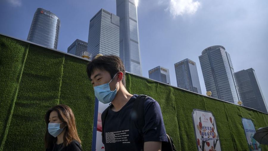 Commuters wearing face masks walk along a street in the central business district in Beijing, Friday, July 29, 2022. (AP Photo/Mark Schiefelbein)
