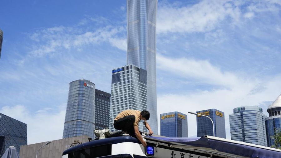 A worker wearing a mask works on a tarpaulin cover near the Central Business District skyline in Beijing, Thursday, July 28, 2022. (AP Photo/Ng Han Guan)