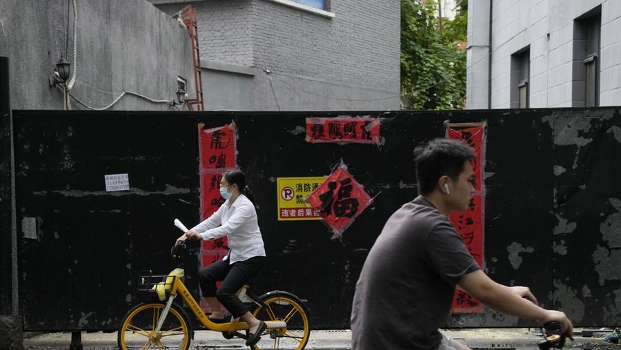 A woman wearing mask cycles past gate with weathered Chinese New Year decorations in Beijing, Thursday, July 28, 2022. (AP Photo/Ng Han Guan)