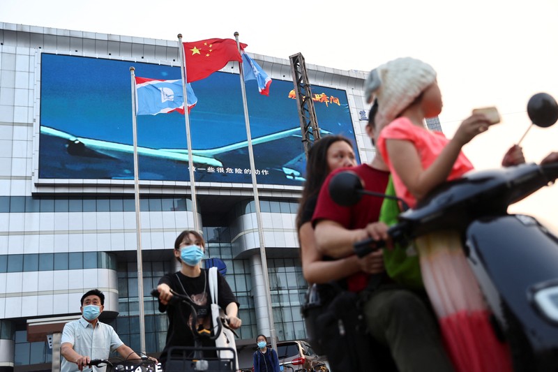 Pedestrians wait at an intersection near a screen showing footage of Chinese People's Liberation Army (PLA) aircraft during an evening news programme, in Beijing, China August 2, 2022. REUTERS/Tingshu Wang