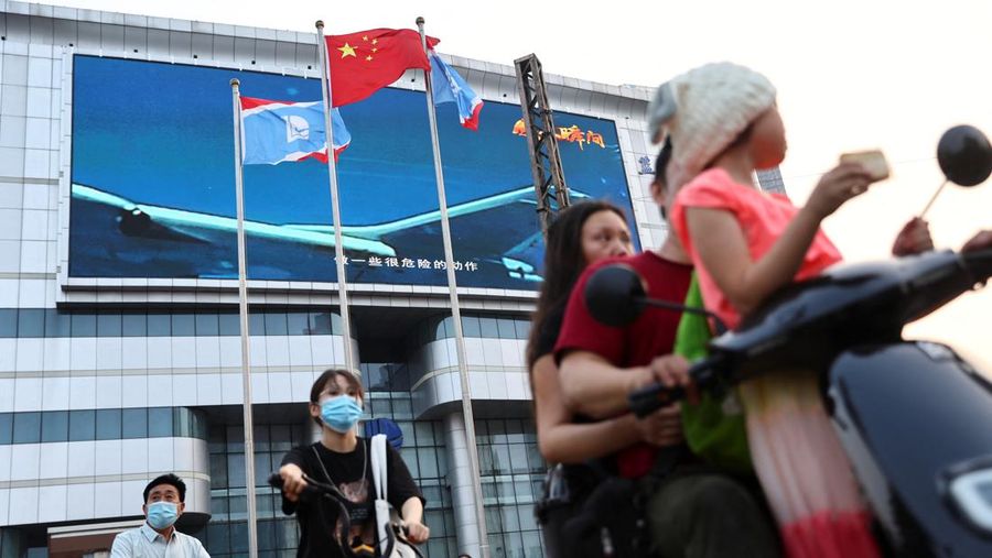 Pedestrians wait at an intersection near a screen showing footage of Chinese People's Liberation Army (PLA) aircraft during an evening news programme, in Beijing, China August 2, 2022. REUTERS/Tingshu Wang