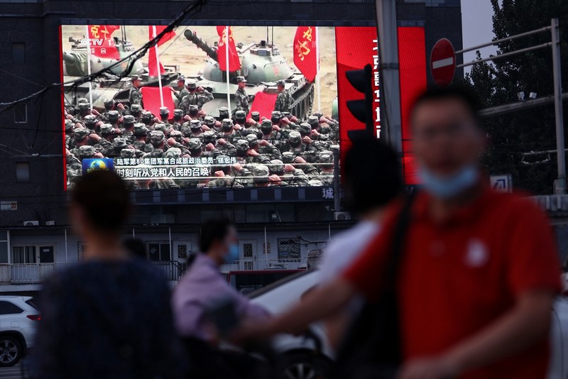 Pedestrians wait at an intersection near a screen showing footage of Chinese People's Liberation Army (PLA) aircraft during an evening news programme, in Beijing, China August 2, 2022. REUTERS/Tingshu Wang