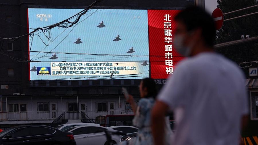 Pedestrians wait at an intersection near a screen showing footage of Chinese People's Liberation Army (PLA) aircraft during an evening news programme, in Beijing, China August 2, 2022. REUTERS/Tingshu Wang