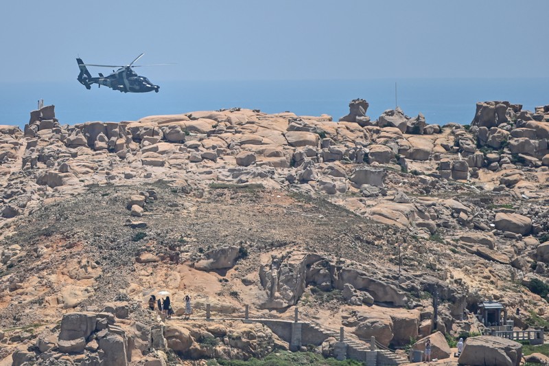 1242294920 Tourists look on as a Chinese military helicopter flies past Pingtan island, one of mainland China's closest point from Taiwan, in Fujian province on August 4, 2022, ahead of massive military drills off Taiwan following US House Speaker Nancy Pelosi's visit to the self-ruled island. - China is due on August 4 to kick off its largest-ever military exercises encircling Taiwan, in a show of force straddling vital international shipping lanes following a visit to the self-ruled island by US House Speaker Nancy Pelosi. (Photo by Hector RETAMAL / AFP) (Photo by HECTOR RETAMAL/AFP via Getty Images)