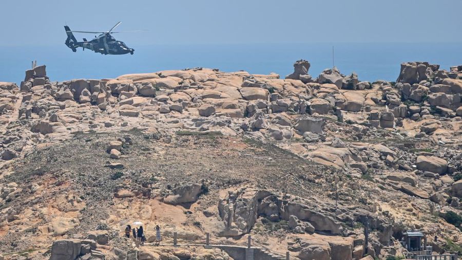 Tourists look on as a Chinese military helicopter flies past Pingtan island, one of mainland China's closest point from Taiwan, in Fujian province on August 4, 2022, ahead of massive military drills off Taiwan following US House Speaker Nancy Pelosi's visit to the self-ruled island. - China is due on August 4 to kick off its largest-ever military exercises encircling Taiwan, in a show of force straddling vital international shipping lanes following a visit to the self-ruled island by US House Speaker Nancy Pelosi. (Photo by Hector RETAMAL / AFP) (Photo by HECTOR RETAMAL/AFP via Getty Images)