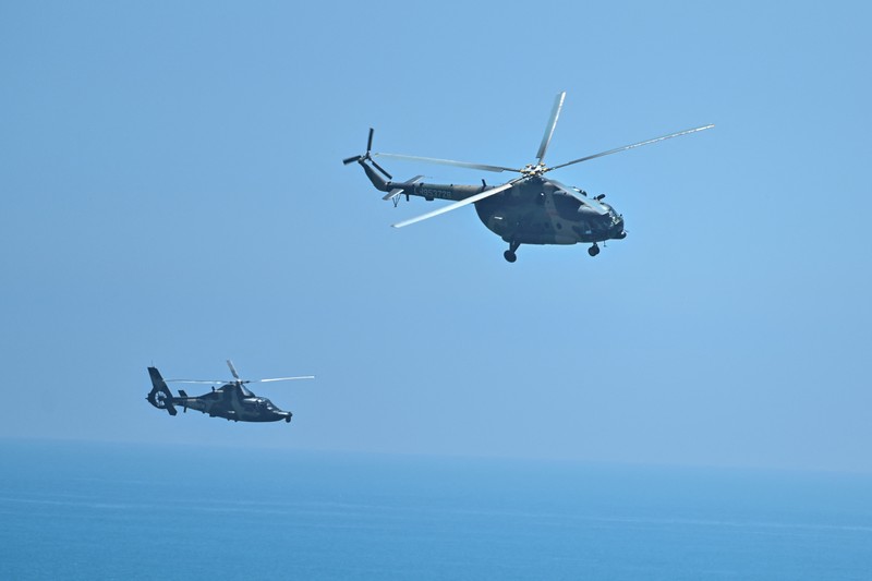 1242294920 Tourists look on as a Chinese military helicopter flies past Pingtan island, one of mainland China's closest point from Taiwan, in Fujian province on August 4, 2022, ahead of massive military drills off Taiwan following US House Speaker Nancy Pelosi's visit to the self-ruled island. - China is due on August 4 to kick off its largest-ever military exercises encircling Taiwan, in a show of force straddling vital international shipping lanes following a visit to the self-ruled island by US House Speaker Nancy Pelosi. (Photo by Hector RETAMAL / AFP) (Photo by HECTOR RETAMAL/AFP via Getty Images)