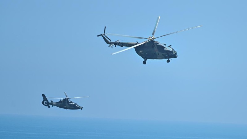 Tourists look on as a Chinese military helicopter flies past Pingtan island, one of mainland China's closest point from Taiwan, in Fujian province on August 4, 2022, ahead of massive military drills off Taiwan following US House Speaker Nancy Pelosi's visit to the self-ruled island. - China is due on August 4 to kick off its largest-ever military exercises encircling Taiwan, in a show of force straddling vital international shipping lanes following a visit to the self-ruled island by US House Speaker Nancy Pelosi. (Photo by Hector RETAMAL / AFP) (Photo by HECTOR RETAMAL/AFP via Getty Images)