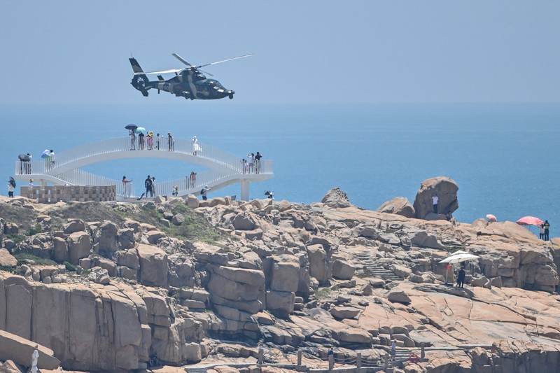 1242294920 Tourists look on as a Chinese military helicopter flies past Pingtan island, one of mainland China's closest point from Taiwan, in Fujian province on August 4, 2022, ahead of massive military drills off Taiwan following US House Speaker Nancy Pelosi's visit to the self-ruled island. - China is due on August 4 to kick off its largest-ever military exercises encircling Taiwan, in a show of force straddling vital international shipping lanes following a visit to the self-ruled island by US House Speaker Nancy Pelosi. (Photo by Hector RETAMAL / AFP) (Photo by HECTOR RETAMAL/AFP via Getty Images)