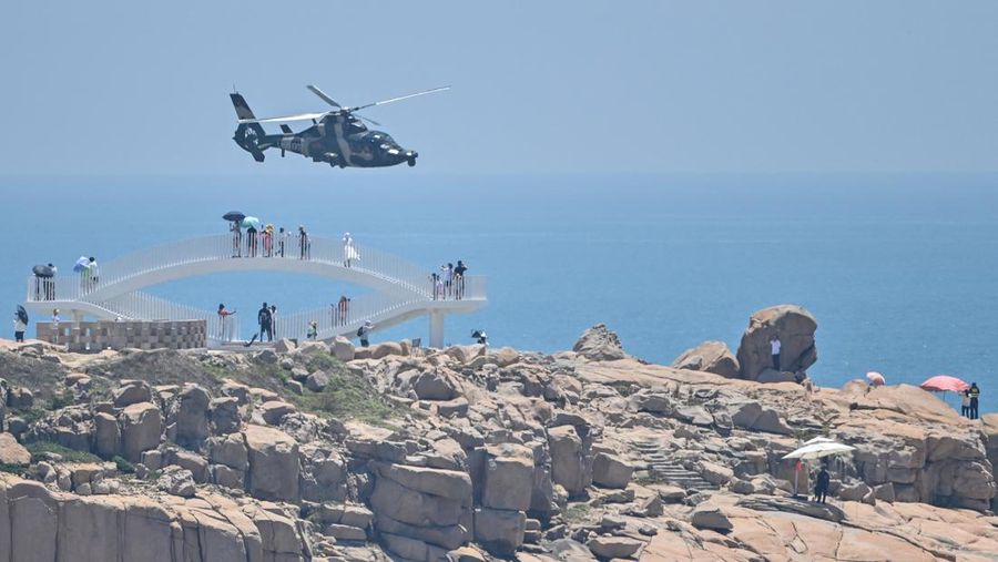 Tourists look on as a Chinese military helicopter flies past Pingtan island, one of mainland China's closest point from Taiwan, in Fujian province on August 4, 2022, ahead of massive military drills off Taiwan following US House Speaker Nancy Pelosi's visit to the self-ruled island. - China is due on August 4 to kick off its largest-ever military exercises encircling Taiwan, in a show of force straddling vital international shipping lanes following a visit to the self-ruled island by US House Speaker Nancy Pelosi. (Photo by Hector RETAMAL / AFP) (Photo by HECTOR RETAMAL/AFP via Getty Images)