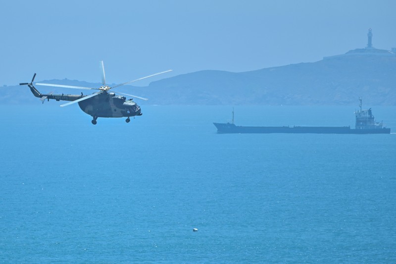 1242294920 Tourists look on as a Chinese military helicopter flies past Pingtan island, one of mainland China's closest point from Taiwan, in Fujian province on August 4, 2022, ahead of massive military drills off Taiwan following US House Speaker Nancy Pelosi's visit to the self-ruled island. - China is due on August 4 to kick off its largest-ever military exercises encircling Taiwan, in a show of force straddling vital international shipping lanes following a visit to the self-ruled island by US House Speaker Nancy Pelosi. (Photo by Hector RETAMAL / AFP) (Photo by HECTOR RETAMAL/AFP via Getty Images)