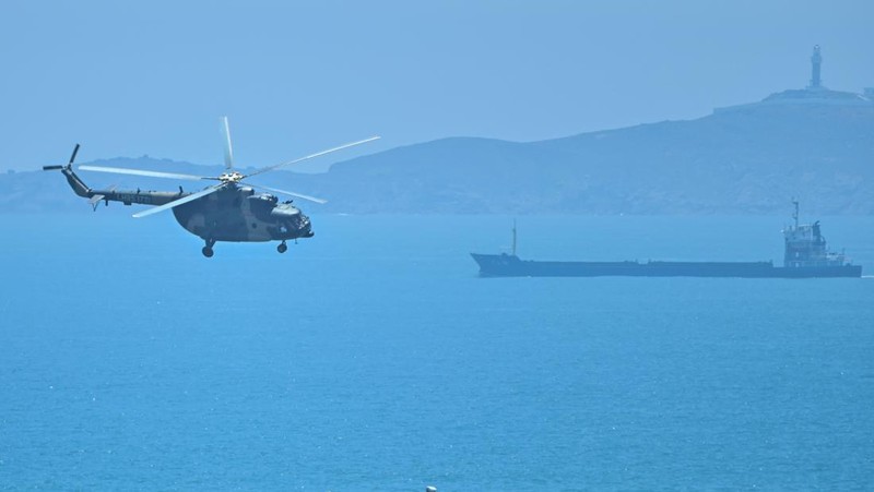 Tourists look on as a Chinese military helicopter flies past Pingtan island, one of mainland China's closest point from Taiwan, in Fujian province on August 4, 2022, ahead of massive military drills off Taiwan following US House Speaker Nancy Pelosi's visit to the self-ruled island. - China is due on August 4 to kick off its largest-ever military exercises encircling Taiwan, in a show of force straddling vital international shipping lanes following a visit to the self-ruled island by US House Speaker Nancy Pelosi. (Photo by Hector RETAMAL / AFP) (Photo by HECTOR RETAMAL/AFP via Getty Images)