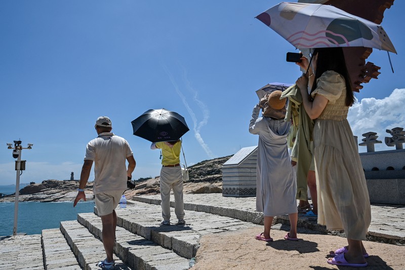Tourists look on as a Chinese military helicopter flies past Pingtan island, one of mainland China's closest point from Taiwan, in Fujian province on August 4, 2022, ahead of massive military drills off Taiwan following US House Speaker Nancy Pelosi's visit to the self-ruled island. - China is due on August 4 to kick off its largest-ever military exercises encircling Taiwan, in a show of force straddling vital international shipping lanes following a visit to the self-ruled island by US House Speaker Nancy Pelosi. (Photo by Hector RETAMAL / AFP) (Photo by HECTOR RETAMAL/AFP via Getty Images)