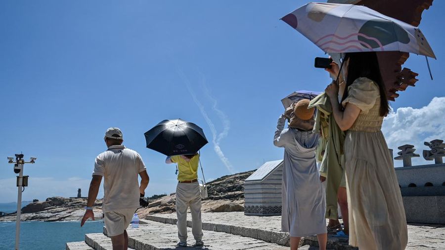 Tourists look on as a Chinese military helicopter flies past Pingtan island, one of mainland China's closest point from Taiwan, in Fujian province on August 4, 2022, ahead of massive military drills off Taiwan following US House Speaker Nancy Pelosi's visit to the self-ruled island. - China is due on August 4 to kick off its largest-ever military exercises encircling Taiwan, in a show of force straddling vital international shipping lanes following a visit to the self-ruled island by US House Speaker Nancy Pelosi. (Photo by Hector RETAMAL / AFP) (Photo by HECTOR RETAMAL/AFP via Getty Images)