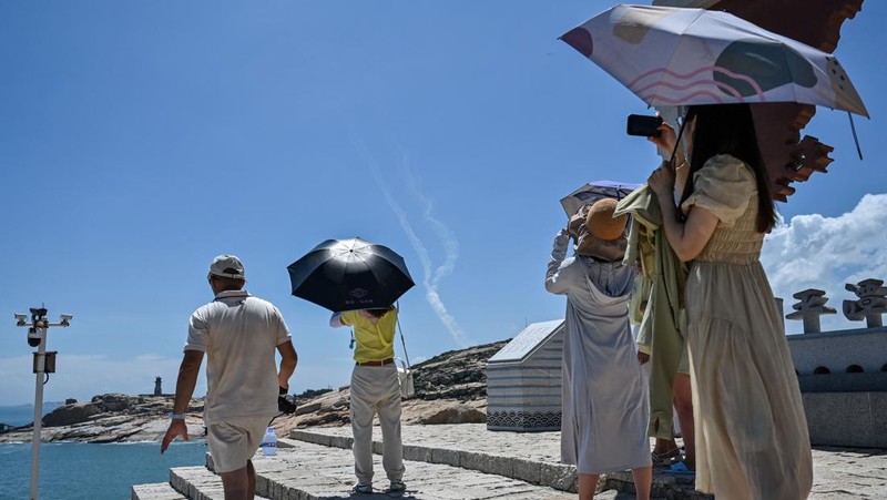 Tourists look on as a Chinese military helicopter flies past Pingtan island, one of mainland China's closest point from Taiwan, in Fujian province on August 4, 2022, ahead of massive military drills off Taiwan following US House Speaker Nancy Pelosi's visit to the self-ruled island. - China is due on August 4 to kick off its largest-ever military exercises encircling Taiwan, in a show of force straddling vital international shipping lanes following a visit to the self-ruled island by US House Speaker Nancy Pelosi. (Photo by Hector RETAMAL / AFP) (Photo by HECTOR RETAMAL/AFP via Getty Images)