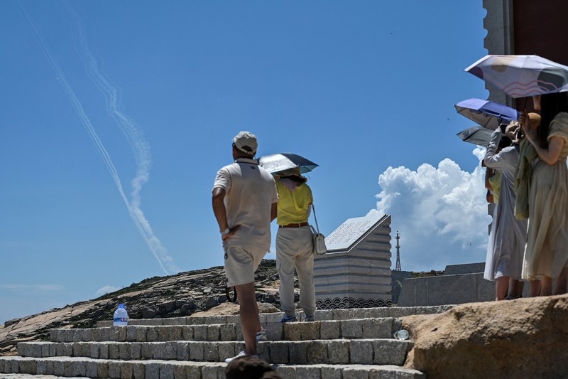 Tourists look on as a Chinese military helicopter flies past Pingtan island, one of mainland China's closest point from Taiwan, in Fujian province on August 4, 2022, ahead of massive military drills off Taiwan following US House Speaker Nancy Pelosi's visit to the self-ruled island. - China is due on August 4 to kick off its largest-ever military exercises encircling Taiwan, in a show of force straddling vital international shipping lanes following a visit to the self-ruled island by US House Speaker Nancy Pelosi. (Photo by Hector RETAMAL / AFP) (Photo by HECTOR RETAMAL/AFP via Getty Images)