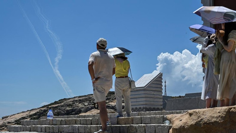 Tourists look on as a Chinese military helicopter flies past Pingtan island, one of mainland China's closest point from Taiwan, in Fujian province on August 4, 2022, ahead of massive military drills off Taiwan following US House Speaker Nancy Pelosi's visit to the self-ruled island. - China is due on August 4 to kick off its largest-ever military exercises encircling Taiwan, in a show of force straddling vital international shipping lanes following a visit to the self-ruled island by US House Speaker Nancy Pelosi. (Photo by Hector RETAMAL / AFP) (Photo by HECTOR RETAMAL/AFP via Getty Images)