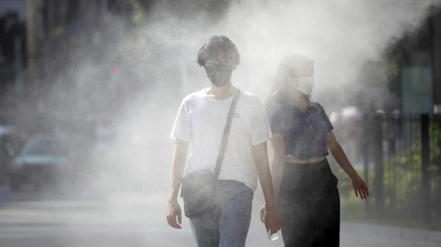 People wearing face masks to help protect against the spread of the coronavirus cool off at a cooling mist spot Monday, Aug. 1, 2022, in Tokyo. Hot weather continues in the metropolitan area as the temperature is expected to rise to 35 degrees Celsius (95 degrees Fahrenheit), according to Japan's meteorological bureau. (AP Photo/Eugene Hoshiko)