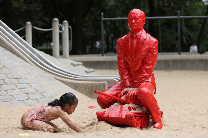Children put sand on a statue of Russian President Vladimir Putin riding a tank created by French artist James Colomina in Central Park in Manhattan, New York City, U.S., August 2, 2022. REUTERS/Andrew Kelly