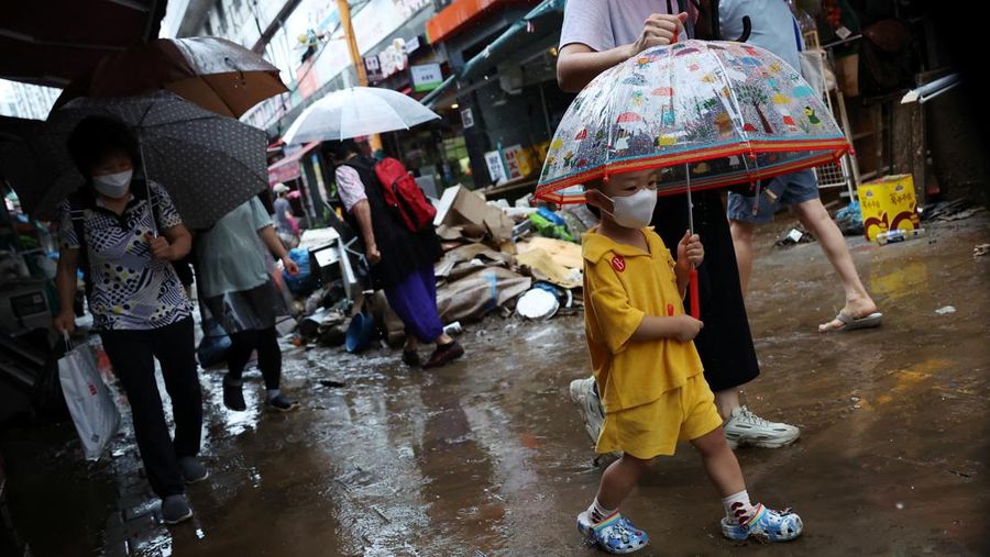 Seorang anak laki-laki menggunakan payung melewati jalan yang tergenang air setelah hujan deras di pasar tradisional di Seoul, Korea Selatan, Selasa (9/8/2022). (REUTERS/Kim Hong-Ji)