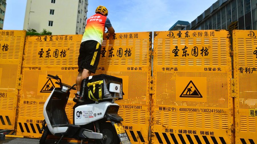 Seorang kurir berdiri di atas sepeda listrik untuk melakukan pengiriman melalui barikade, di tengah tindakan penguncian untuk mengekang wabah penyakit coronavirus (COVID-19) di Sanya, provinsi Hainan, China, Sabtu (6/8/2022). (China Daily via REUTERS)