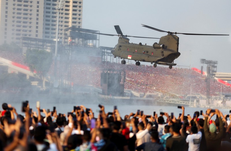 Perayaan Hari Nasional di Singapura Penonton bersorak saat helikopter Chinook Angkatan Udara Singapura dikawal oleh helikopter Apache berparade dengan bendera Singapura untuk menandai Hari Nasional ke-57 negara itu, di Singapura, Selasa (9/8/2022). (Photo by ROSLAN RAHMAN/AFP via Getty Images)